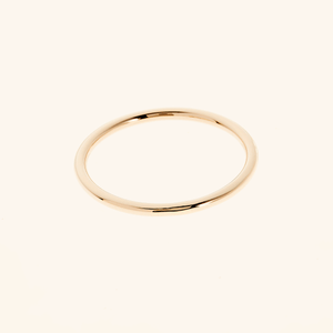 Simple thin gold band ring photographed flat on a soft neutral background.
