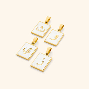 A flat lay of four Arabic letter charms in 18K gold plating, each featuring an iridescent pearl backdrop. The charms are engraved with Arabic letters.