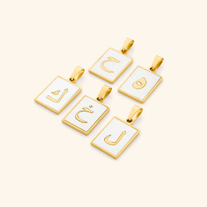 A flat lay of five Arabic letter charms in 18K gold plating, each featuring an iridescent pearl backdrop. The charms are engraved with Arabic letters.