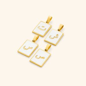 A flat lay of four Arabic letter charms in 18K gold plating, each featuring an iridescent pearl backdrop. The charms are engraved with Arabic letters.
