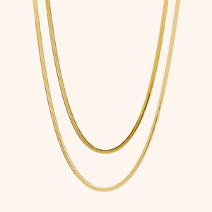 Two gold herringbone chains laid flat against a cream background.