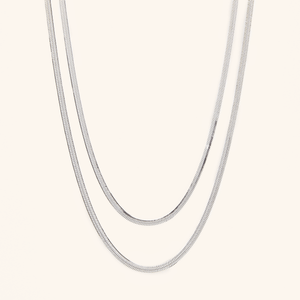Two silver herringbone chains laid flat against a cream background.