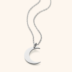 Flat lay of silver minimalist necklace that features a crescent pendant against a light background.