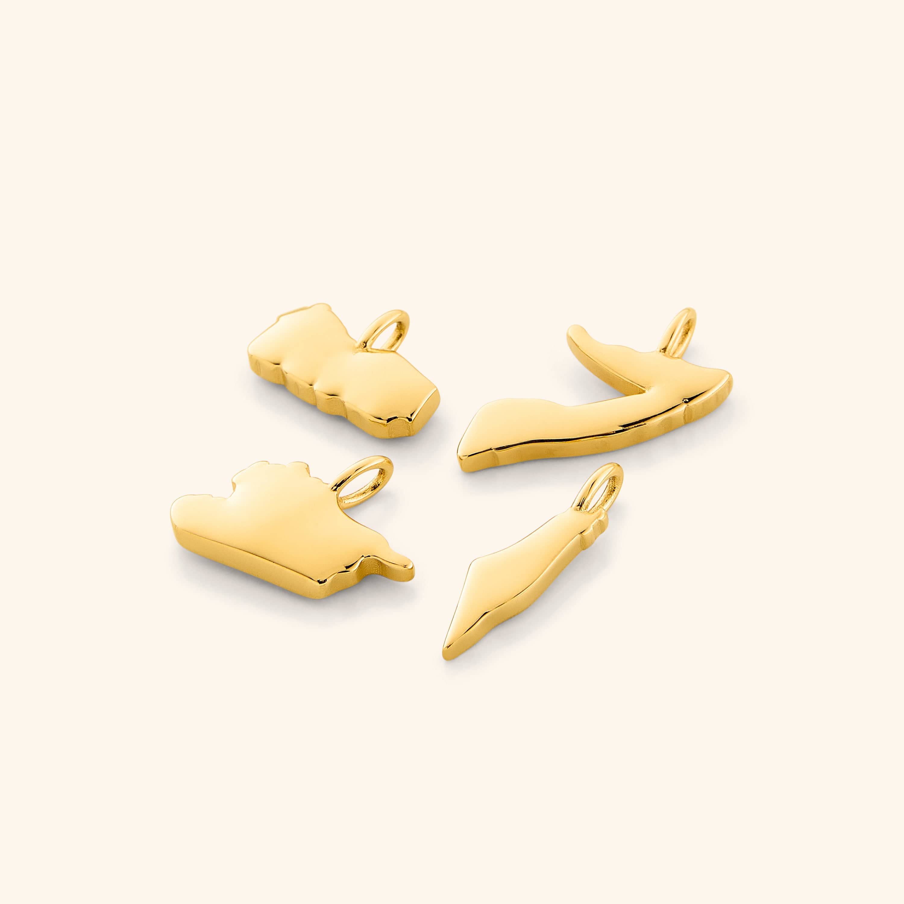 A close-up image showing four gold-plated country map charms arranged side by side on a neutral background, each charm displaying detailed and distinct geographic outlines.