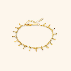 A close-up of the Dangling Dotted Anklet in 18K gold plating. The anklet features a delicate curb chain with evenly spaced 3mm ball-shaped charms that dangle, creating a subtle and elegant design.