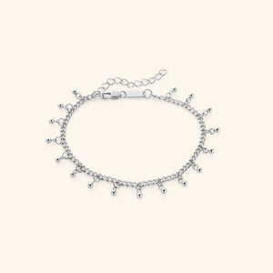 The Dangling Dotted Anklet in a polished silver finish. The anklet showcases a delicate curb chain with evenly spaced 3mm ball-shaped charms that dangle, offering a minimalist and elegant aesthetic.