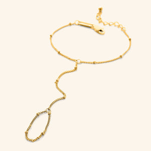 Flat lay of a gold dotted hand chain with a slim bracelet attached to a matching finger loop by a fine chain.