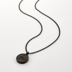 Black necklace with a circular pendant engraved with 'Maktub' calligraphy, displayed on a white background.