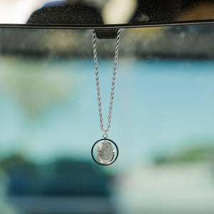 Close-up of a silver car hanger with a circular pendant engraved in Arabic calligraphy of the Shahada.