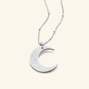 The Ayatul Kursi Crescent Necklace in a polished silver finish, showcasing a crescent pendant adorned with detailed Arabic inscriptions, hanging from a fine silver chain.