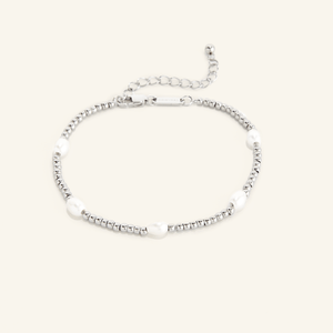 Silver anklet with small round beads and five evenly spaced white pearls, shown on a cream background with an adjustable clasp and extender chain engraved with 'NOMINAL'.