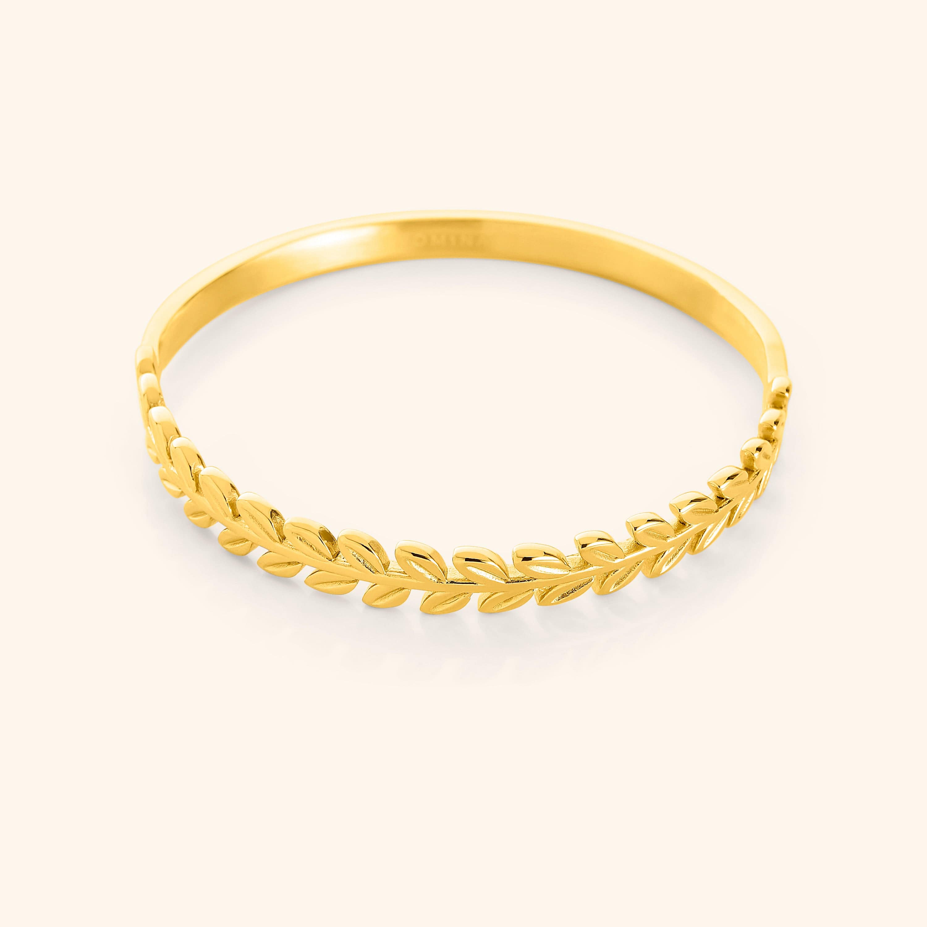 A close-up of the Palestine Olive Layering Bangle in 18K gold plating. The bangle features a delicately twisted olive branch design along one half, symbolizing peace and strength, while the other half remains sleek and unadorned for a modern balance.