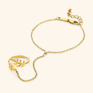 A close-up of the Shining Olive Hand Chain in 18K gold plating. The hand chain features a chain connecting a ring adorned with an olive leaf design to a bracelet.