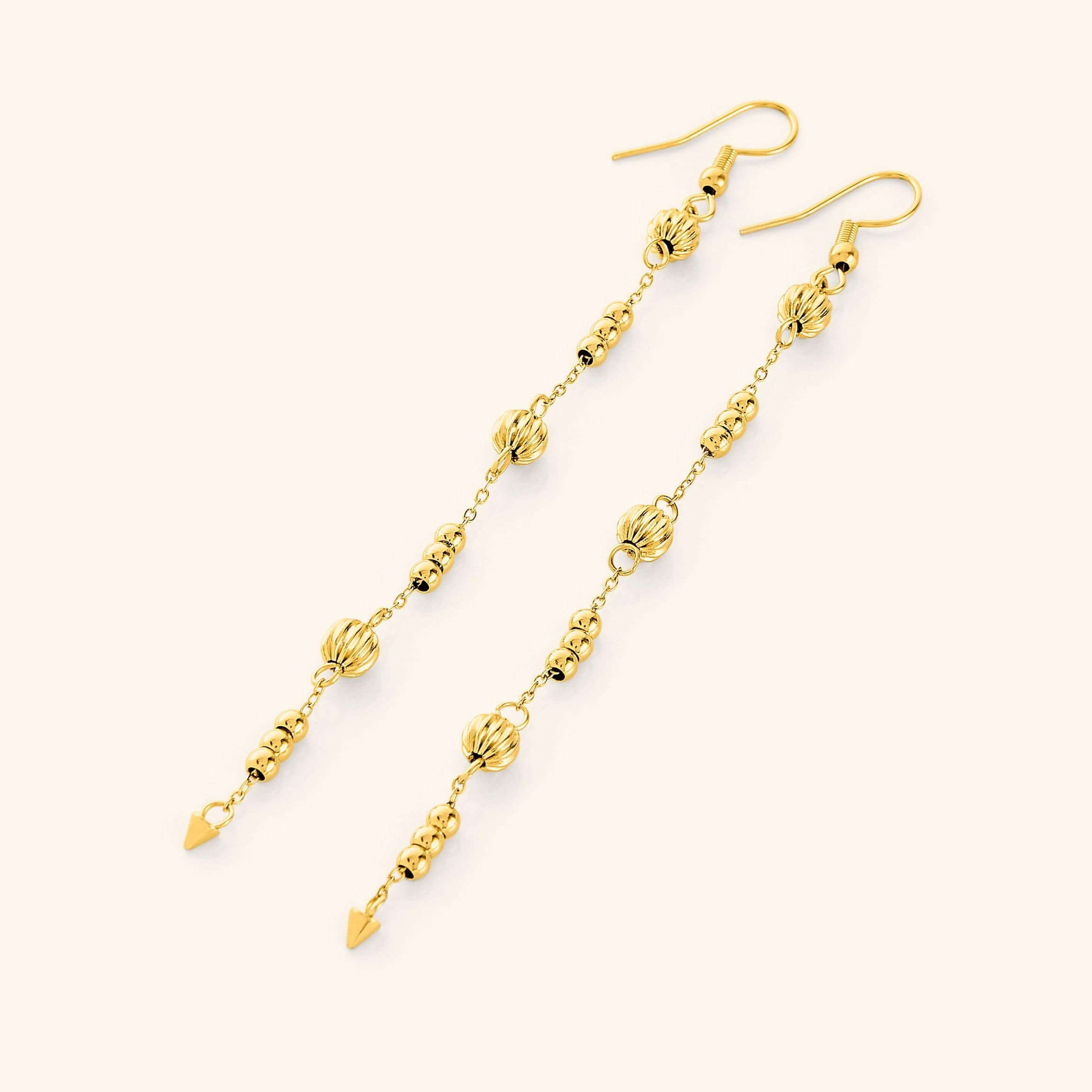 Flat lay of the 18k gold plated earrings. Comet Earrings drop 3.5 inches with delicate, evenly spaced orbs.
