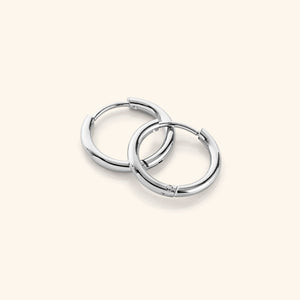 a pair of silver Huggie Essential Hoops | 12mm against a light background.