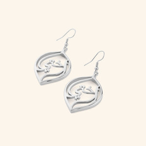 A pair of silver earrings with a droplet framing the Arabic word for "my sister", أختي (ukhti).