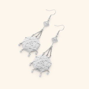 A pair of silver dangling earrings Engraved with the iconic patterns of the mosaic tiles in Syrian homes and fabrics finished with orbs at the bottom of the pendant.