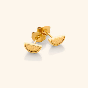 A close-up of the Watermelon Studs in 18K gold plating. Each earring features a small, semi-circular watermelon slice design with red enamel, black seeds, and green rind detailing, symbolizing the Palestinian flag colors.
