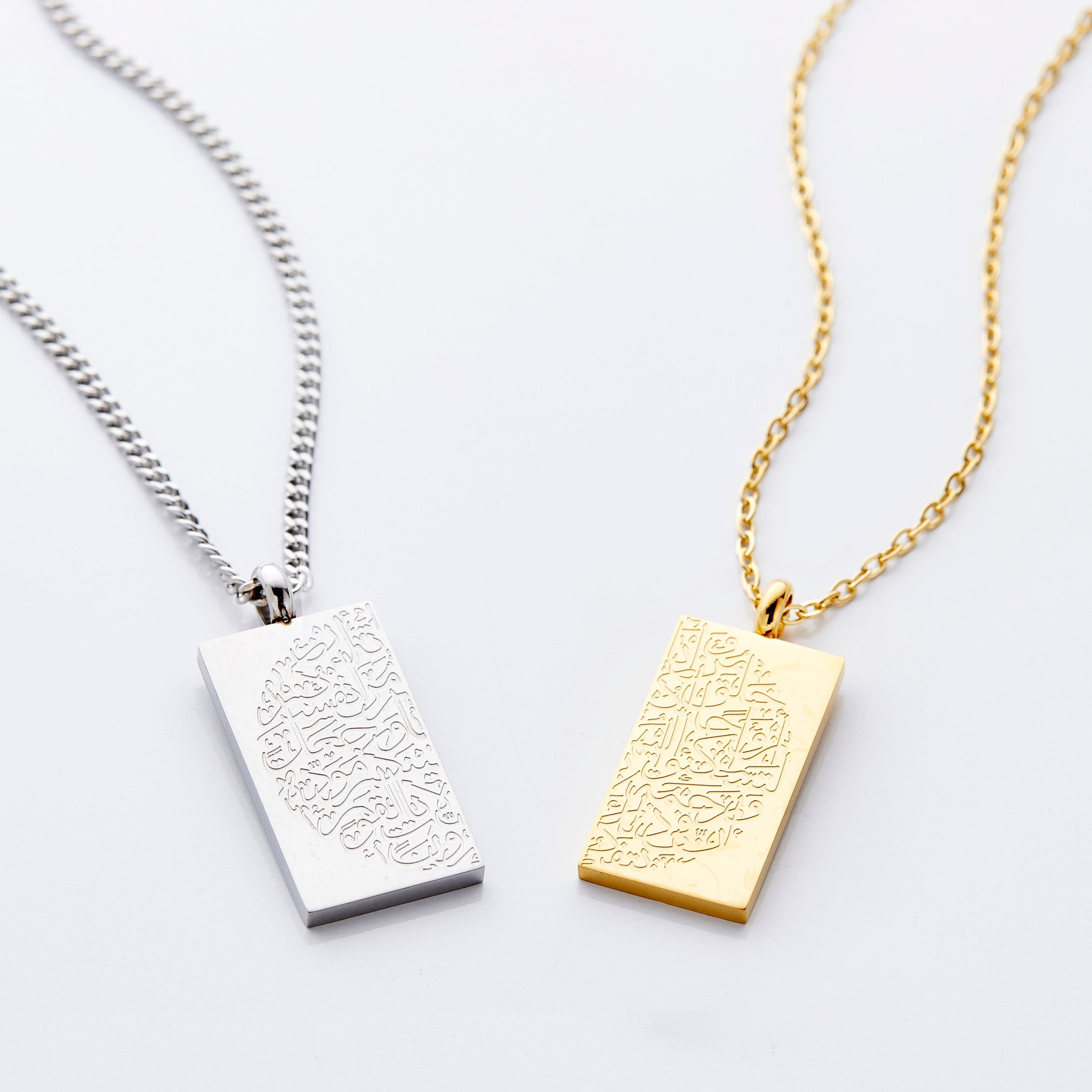 Flat lay of silver and gold necklaces featuring an intricate engraving that complete itself when the pendants are held together, these pieces contain the Arabic calligraphy that translates to And of His signs is that He created for you from yourselves mates that you may find tranquility in them; and He placed between you affection and mercy. Indeed, in that, are signs for a people who reflect. (Quran 30:21)