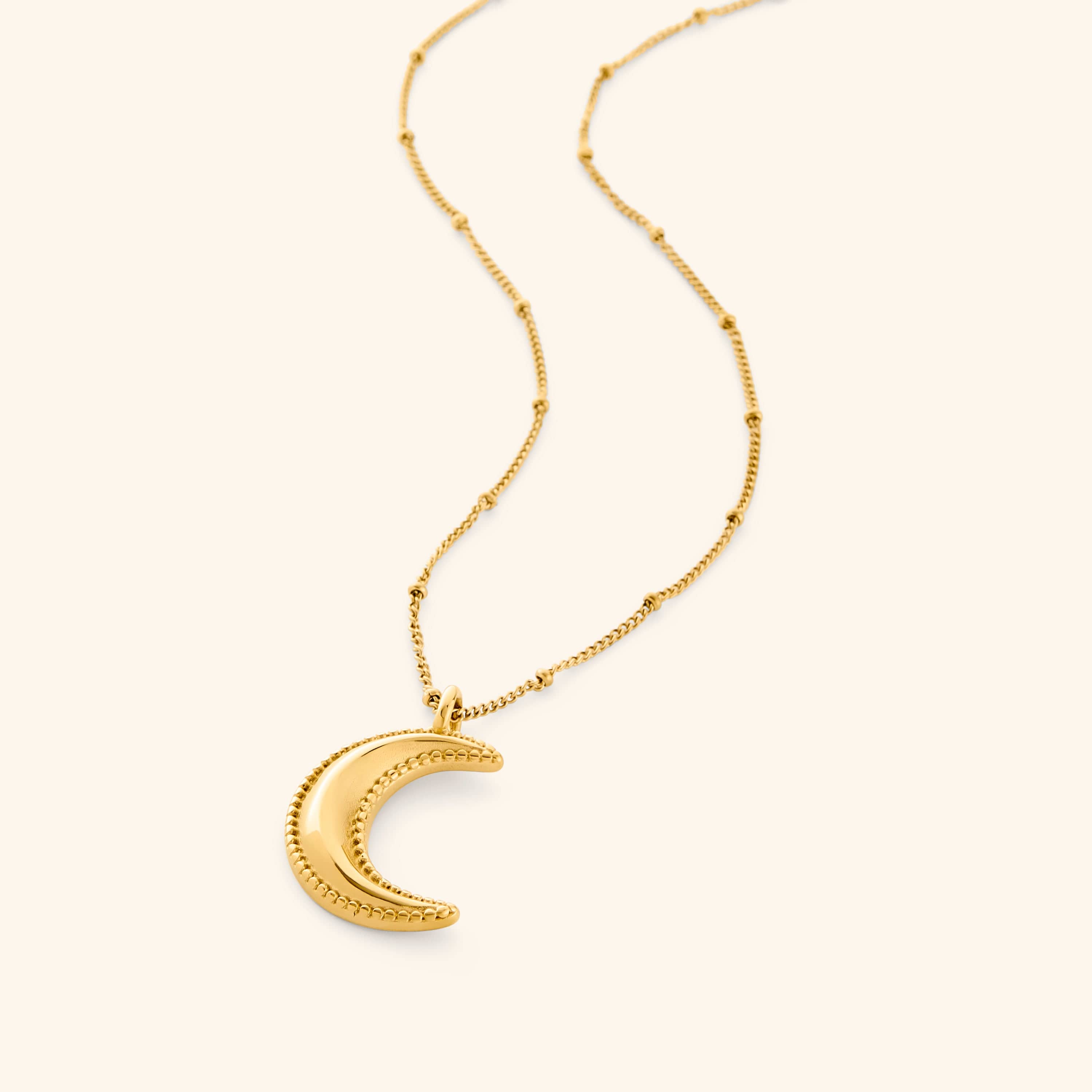 Gold necklace with a dotted crescent moon pendant on a white background