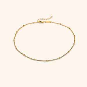 Gold choker with evenly spaced tiny beads, laid flat on a soft beige background.