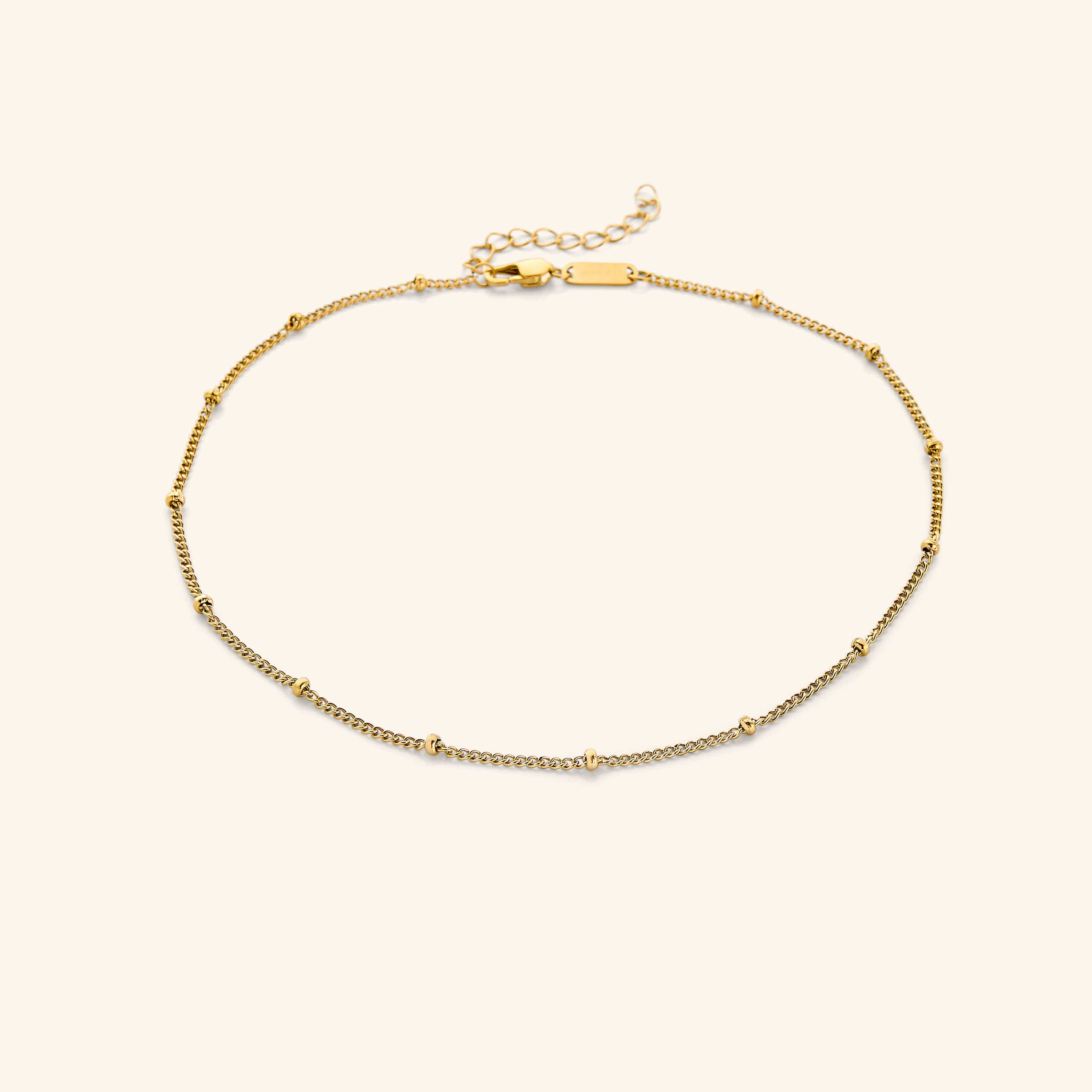 Gold choker with evenly spaced tiny beads, laid flat on a soft beige background.