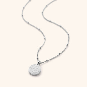 Flat lay of the silver My Sister Necklace against a white background. Sister Necklace features "my sister" inscribed in Arabic (أختي) on a dainty token, finished with a dotted chain.