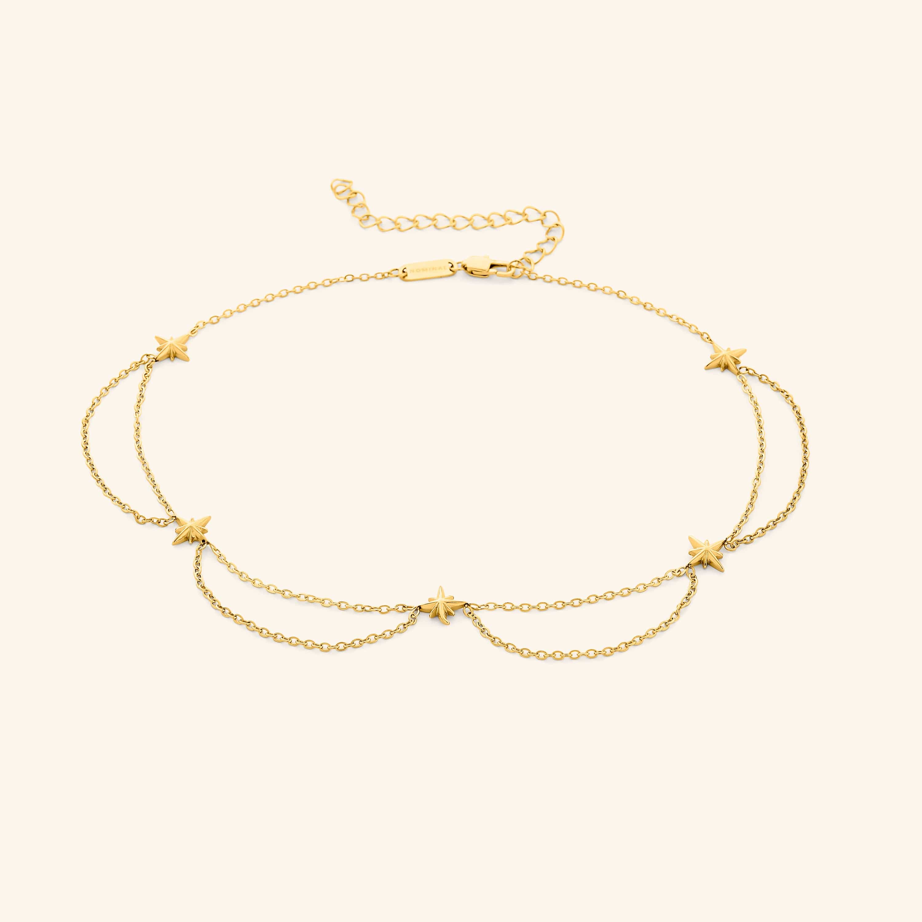 Flat lay of the 18k gold plated necklace that features north stars all along the chain, drooping chains connecting each one.