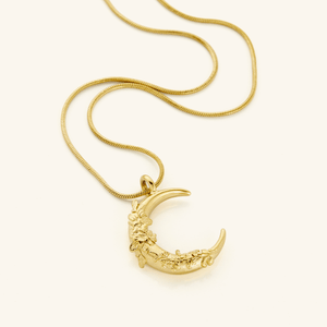 A close-up of the Jasmine Crescent Necklace in 18K gold plating, featuring a crescent-shaped pendant intricately adorned with a jasmine vine design, suspended from the Harmony Chain.