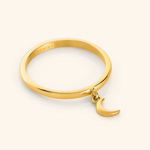 Close-up of a gold ring with a small dangling crescent moon charm attached to the band.