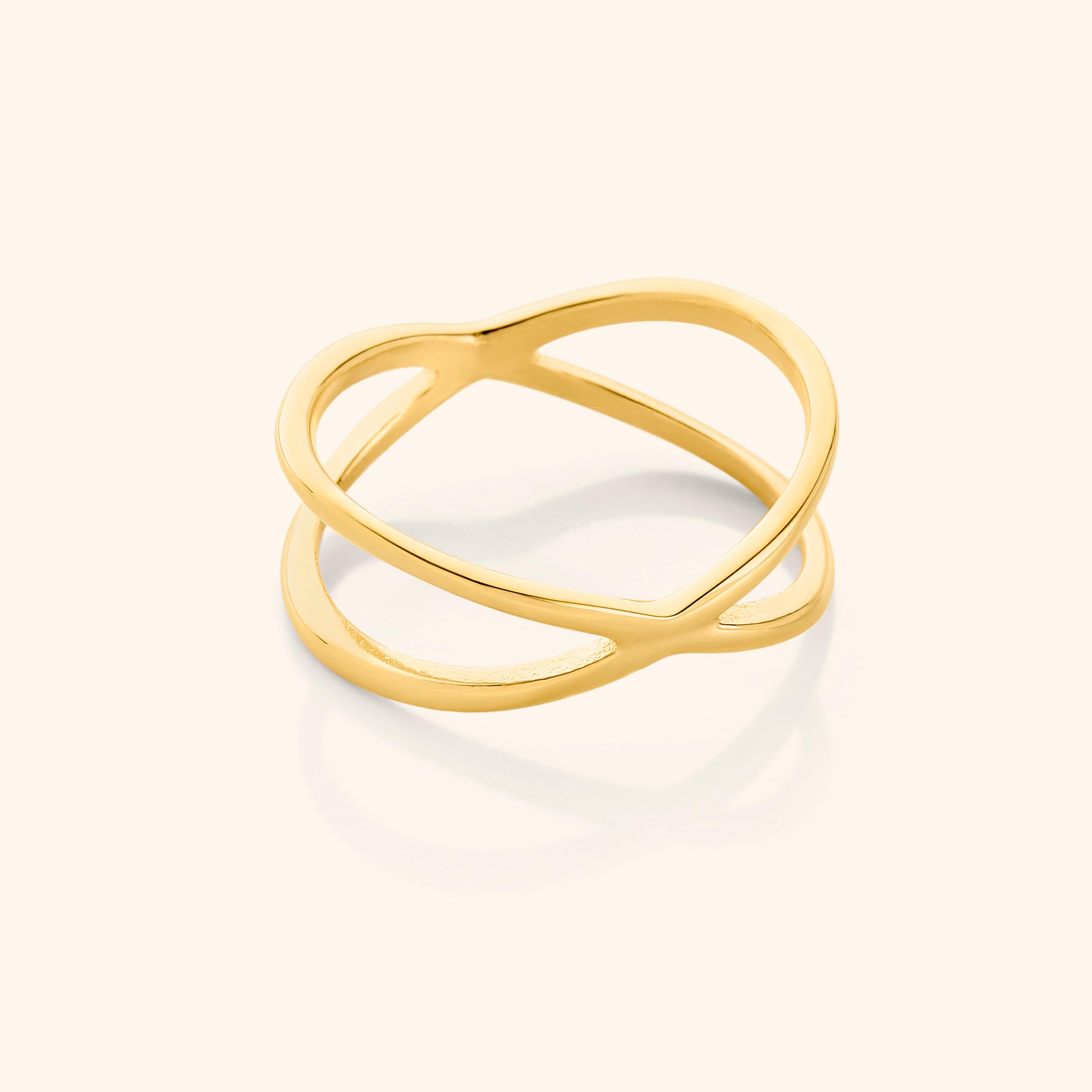 Close-up of a gold essential intersection ring on a neutral background, showcasing its criss-cross double-band design.