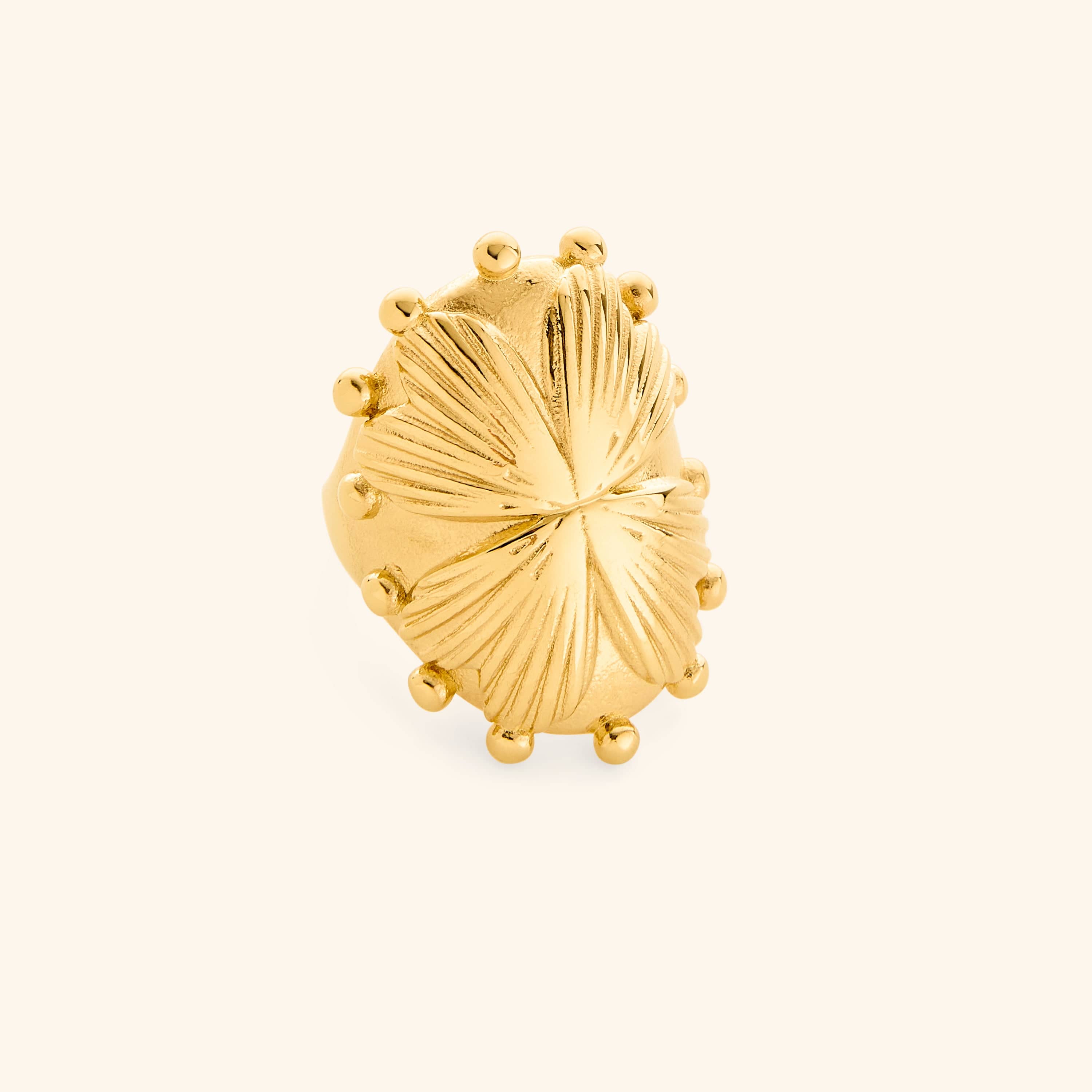 Close-up of a large gold statement ring with textured leaf design and raised bead accents.