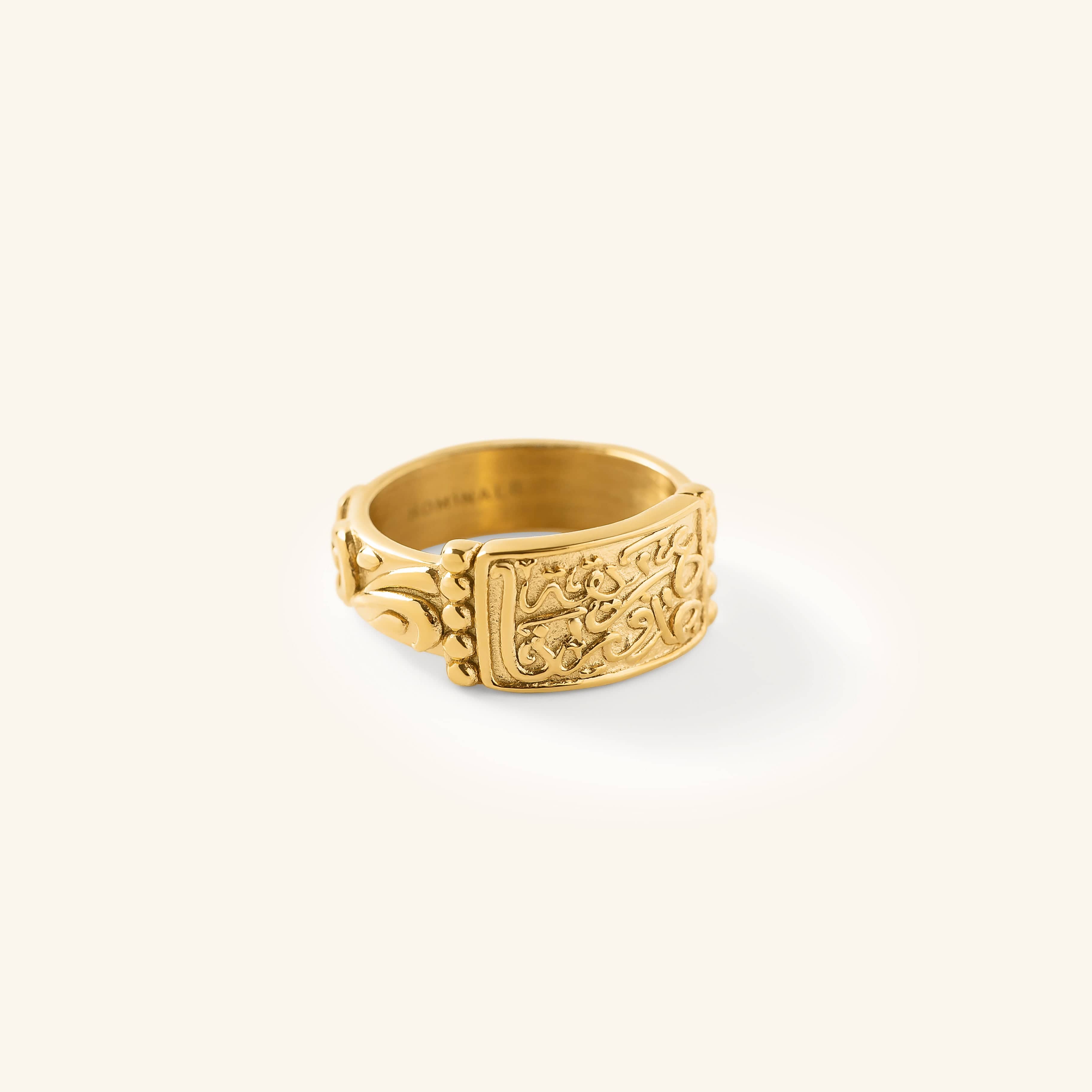 Gold “Our Roots Run Deep” Ring featuring raised Arabic calligraphy and textured detailing across a wide band, shown against a neutral background.