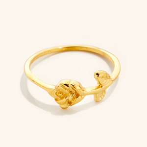 Gold ring featuring a delicate rose design with carved petals and leaves on a slim band, photographed against a neutral background.