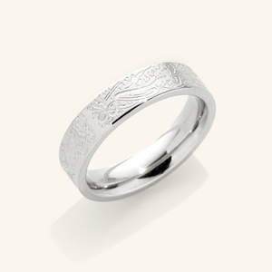 A silver ring with an intricate design etched around the outer surface. The design appears to be Arabic script meaning "With Hardship Comes Ease". The ring is displayed on a bright background with a soft shadow underneath.
