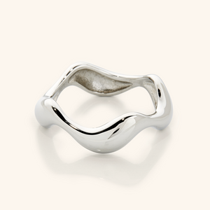 Close-up of a polished silver ring with a sculpted wavy band, photographed against a neutral background.