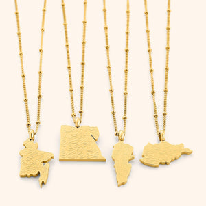 Four gold "With Hardship Comes Ease" Map Necklaces displayed side by side on a white background, each featuring a unique map-shaped pendant engraved with Arabic calligraphy, highlighting variations in map designs and delicate gold chains.
