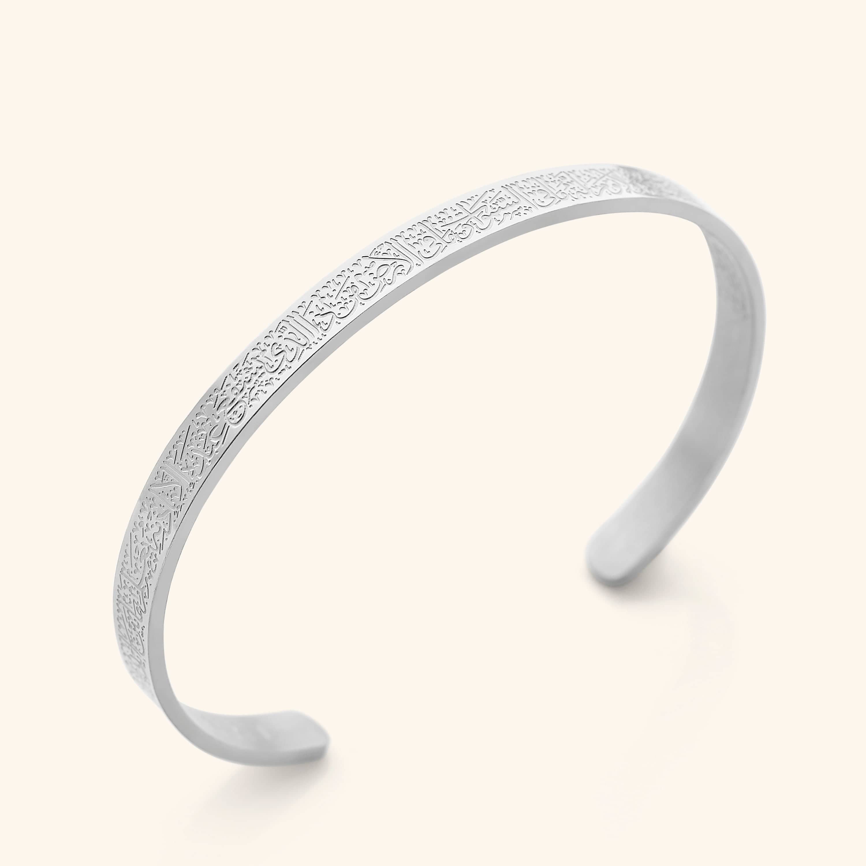 A silver, open-cuff bangle bracelet with an intricate, repeating pattern of Arabic script around its entire outer surface. The bracelet is displayed on a light beige background.