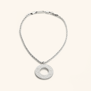 Silver car hanger with a circular pendant engraved in Arabic calligraphy reading “With Hardship Comes Ease,” displayed against a cream background.