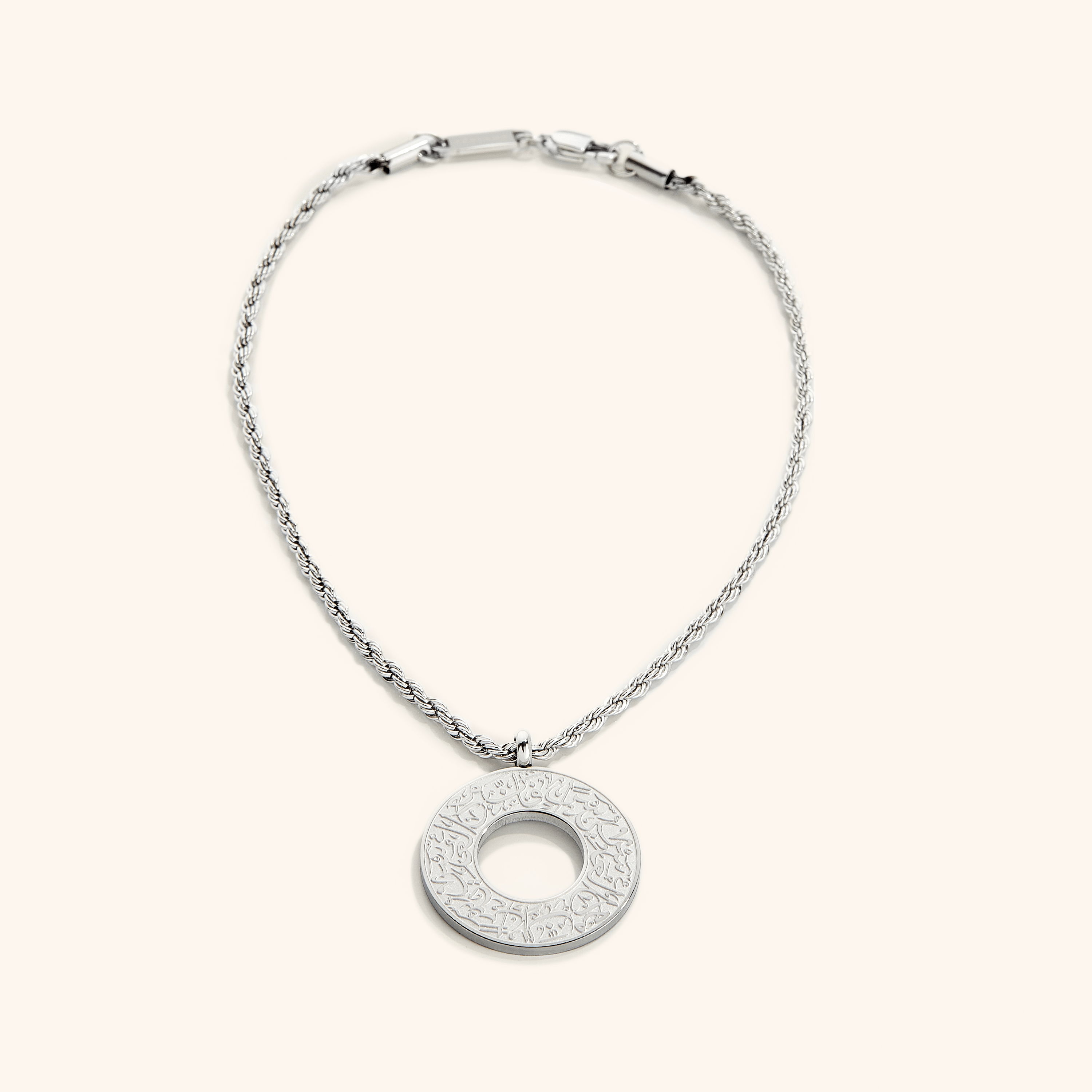 Silver car hanger with a circular pendant engraved in Arabic calligraphy reading “With Hardship Comes Ease,” displayed against a cream background.