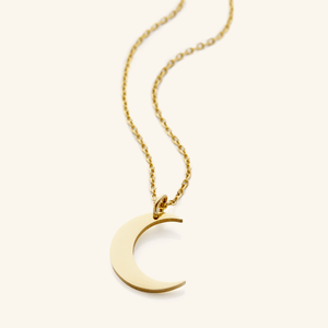 Flat lay of an 18k gold plated minimalist necklace that features a crescent pendant against a light background.