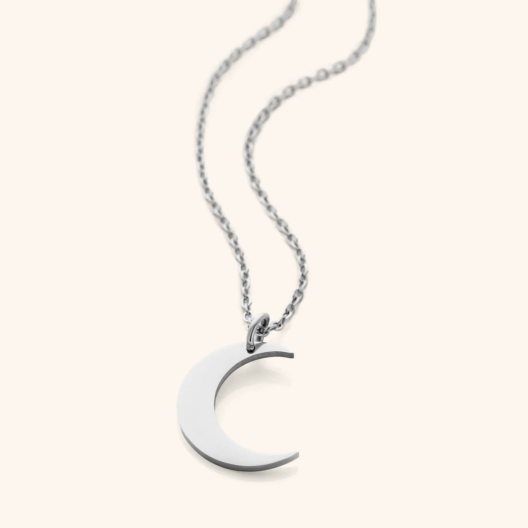 Flat lay of silver minimalist necklace that features a crescent pendant against a light background.