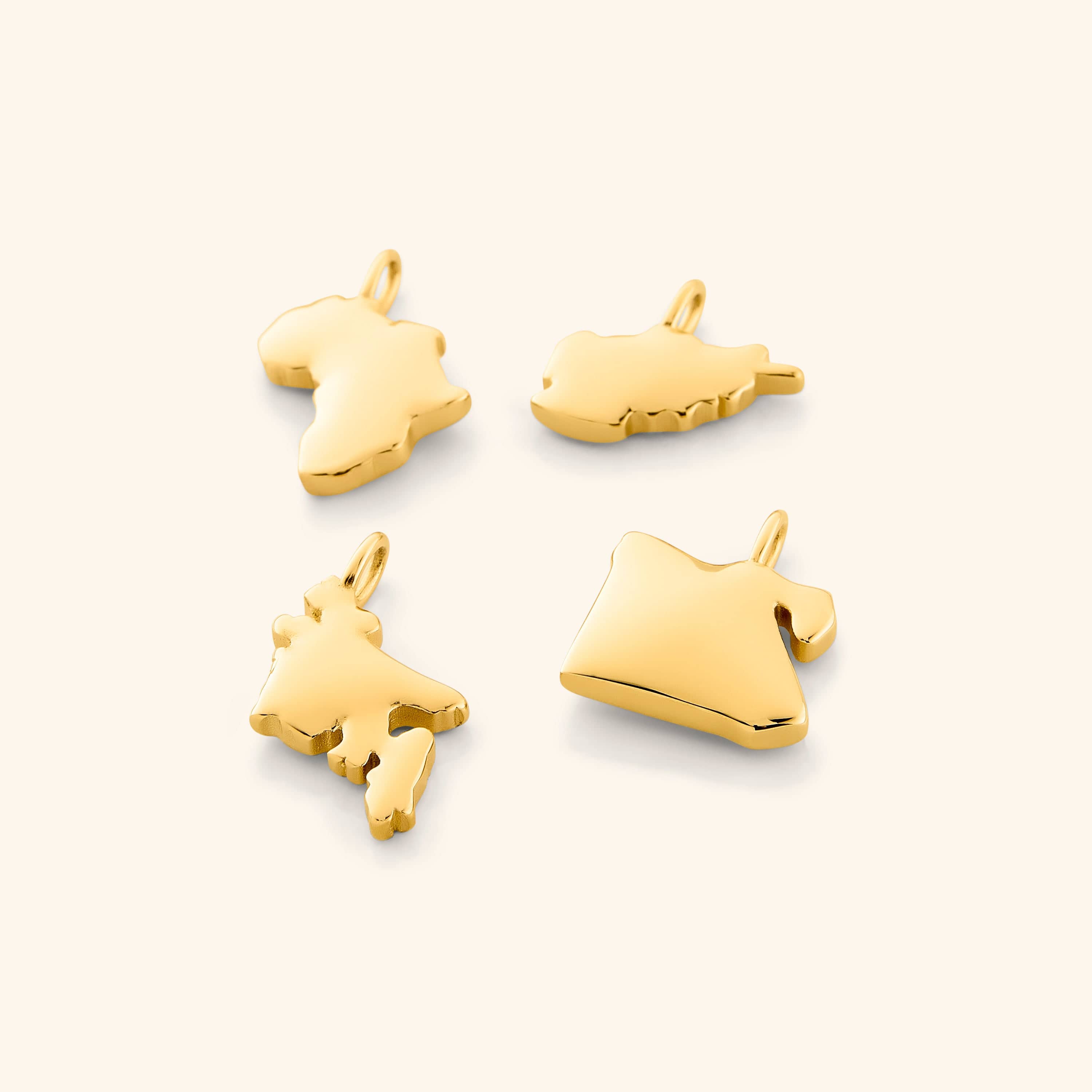 A close-up image showing four gold-plated country map charms arranged side by side on a neutral background, each charm displaying detailed and distinct geographic outlines.