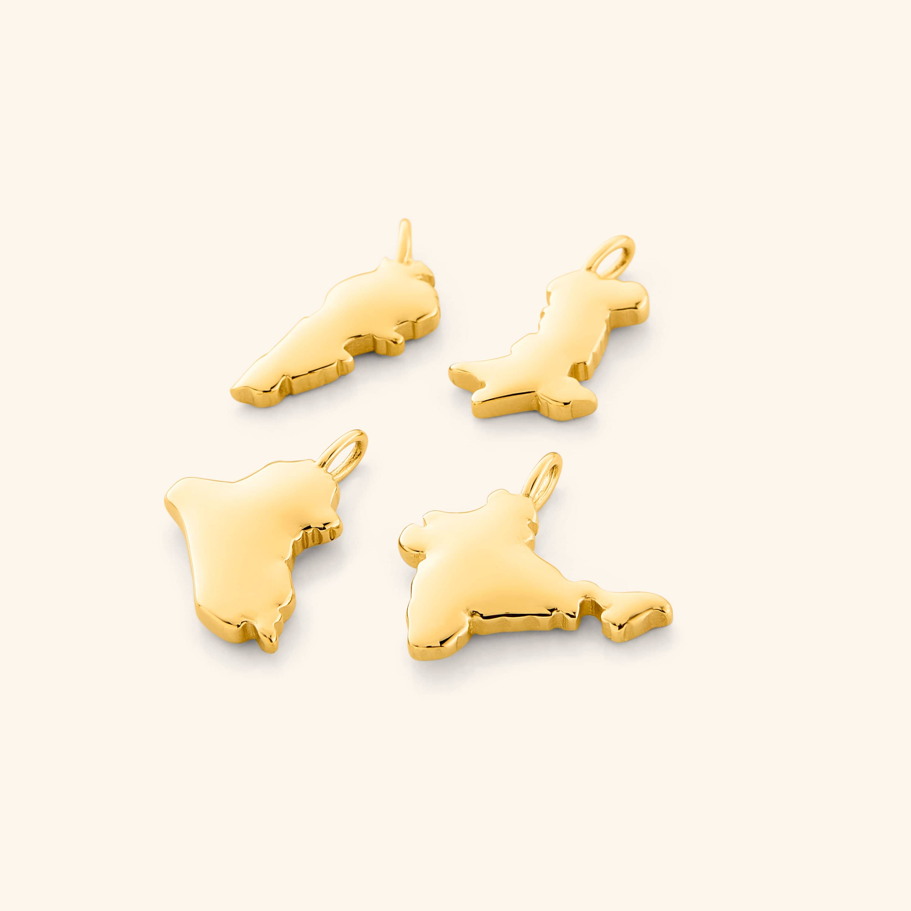 A close-up image showing four gold-plated country map charms arranged side by side on a neutral background, each charm displaying detailed and distinct geographic outlines.