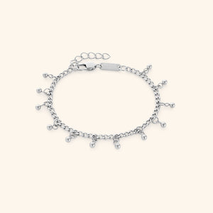 Flat lay of a silver dangling dotted bracelet featuring small dangling beads, displayed against a cream background. The clasp tag shows the engraved text “NOMINAL”.