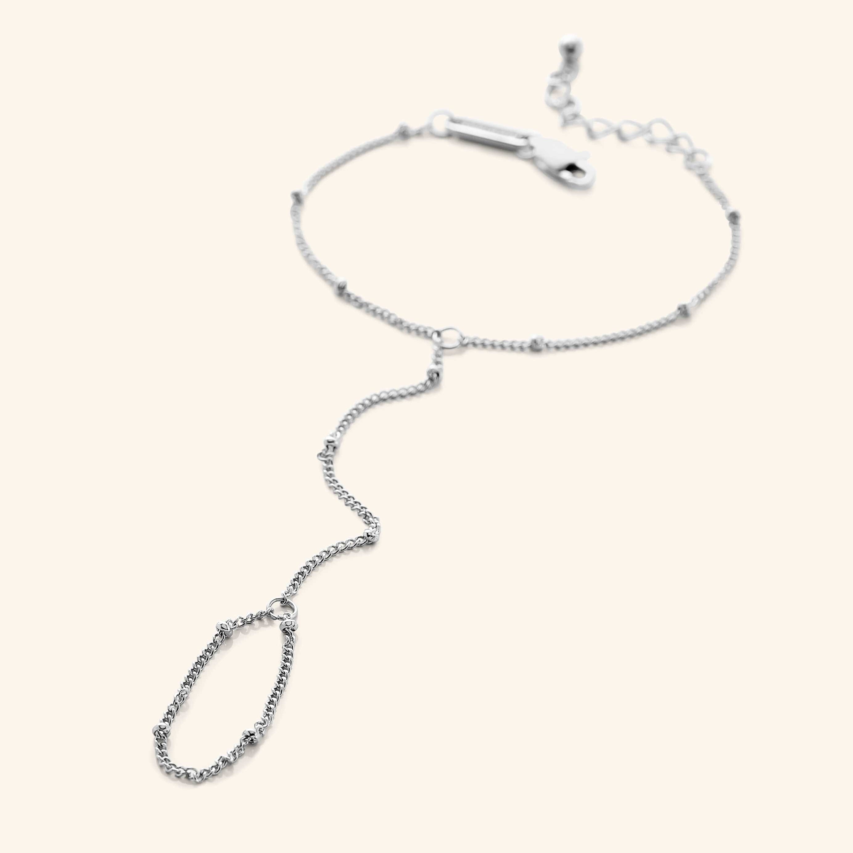 Flat lay of a  silver dotted hand chain with a slim bracelet attached to a matching finger loop by a fine chain.
