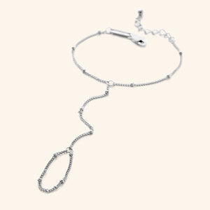 Flat lay of a  silver dotted hand chain with a slim bracelet attached to a matching finger loop by a fine chain.