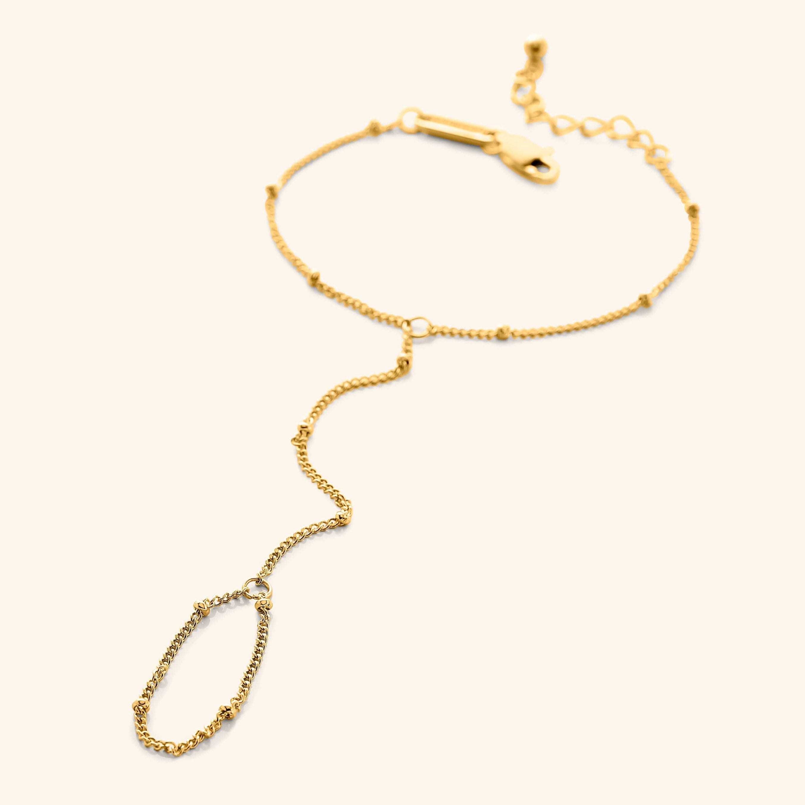 Flat lay of a  gold dotted hand chain with a slim bracelet attached to a matching finger loop by a fine chain.