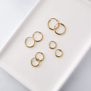 Flat lay of four pairs of gold hoop earrings in various sizes, laid out neatly on a white ceramic tray.