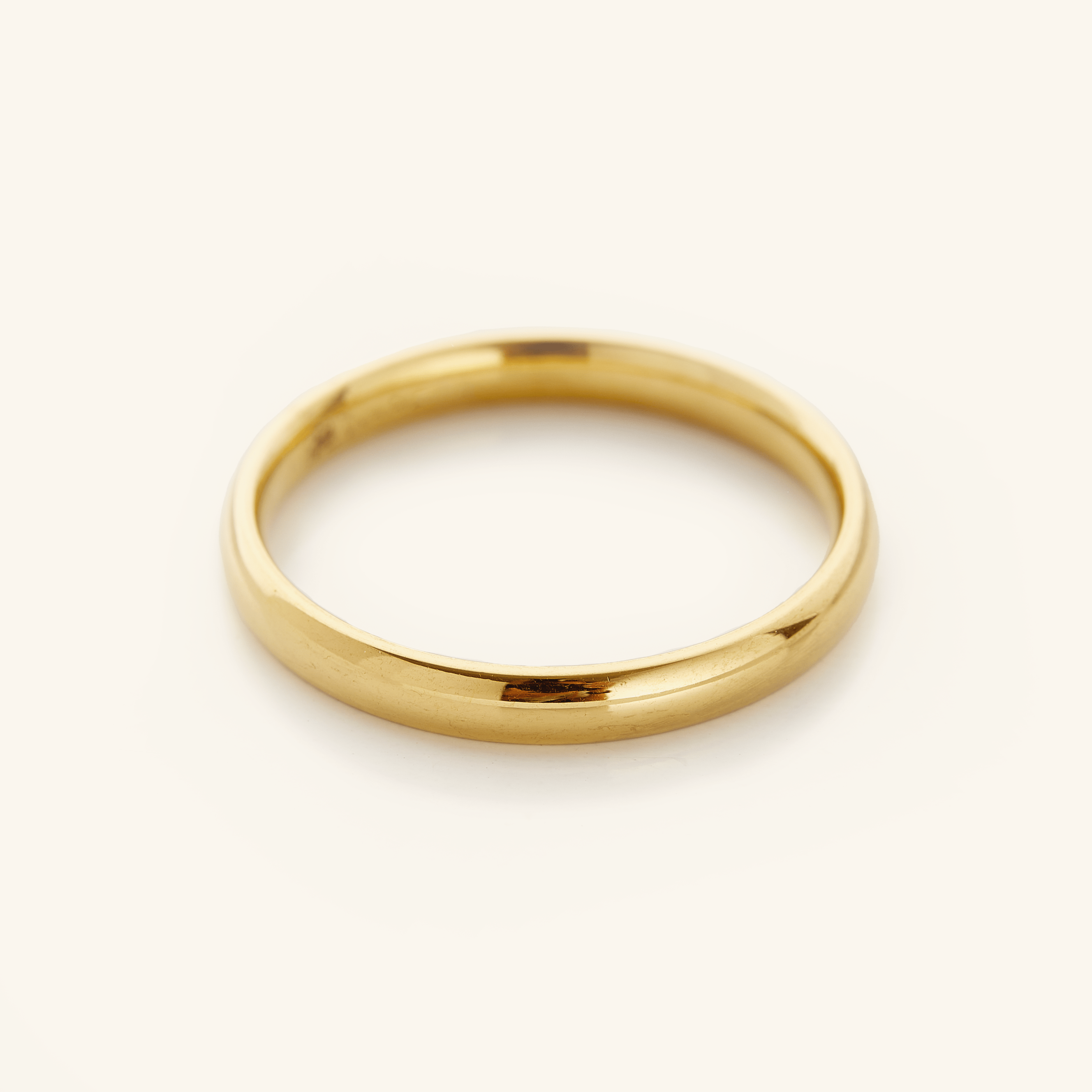 Gold band ring displayed on a soft cream background.